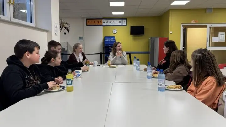 Jugendliche und Erwachsene sitzen beim Frühstück an einem langen Tisch in der Mensa im Gespräch