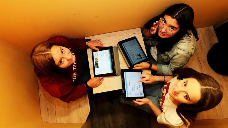 Drei Schülerinnen von oben fotografiert, sie arbeiten an einem Tisch mit Tablets