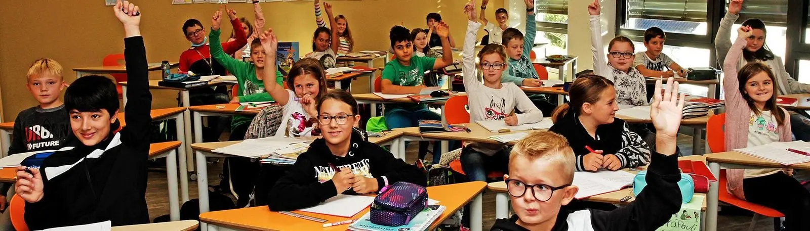 Klasse im Unterricht, viele Schülerinnen und Schüler melden sich mit erhobener Hand