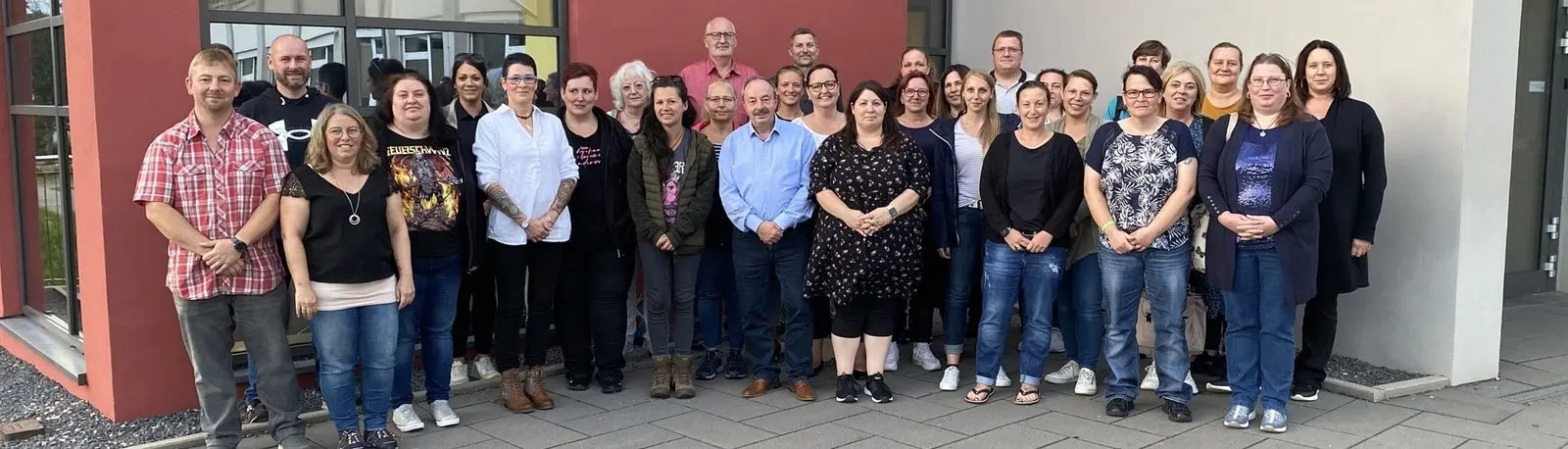 Gruppenfoto von rund drei Dutzend Erwachsenen vor einem Gebäude mit roter Fassade