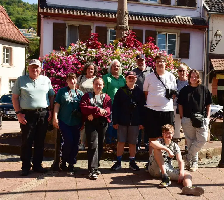 Gruppenfoto von Jugendlichen mit Kameras und Erwachsenen vor einem blumengeschmückten Brunnen