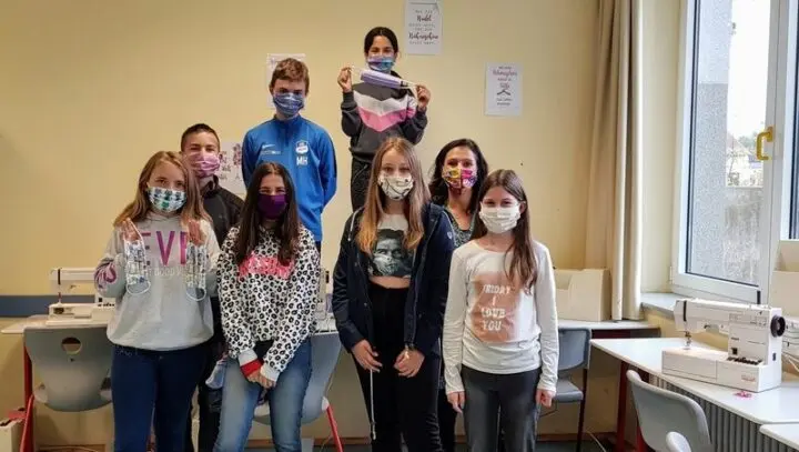 Schülerinnen und Schüler mit selbst genähten Masken im Raum mit Nähmaschinen