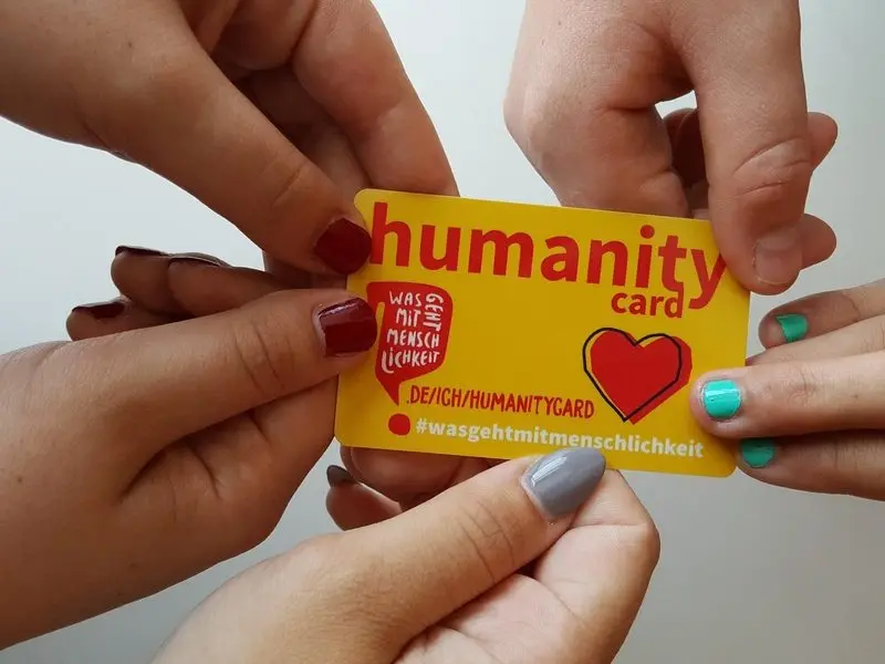 Mehrere Hände halten eine gelbe Humanity Card
