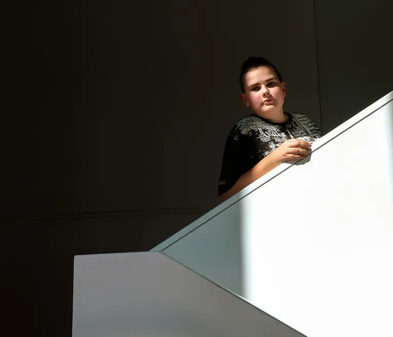 Fotografie: Junge lehnt im Treppenhaus an einem weißen Geländer, starker Hell-Dunkel-Kontrast