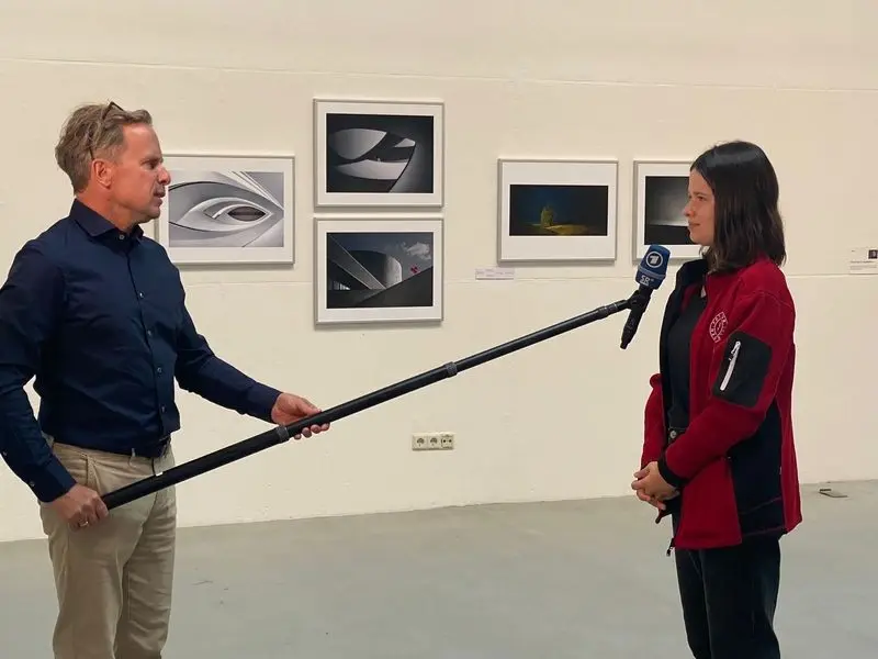 Fernsehinterview mit einer Jugendlichen in roter Jacke in einer Fotoausstellung