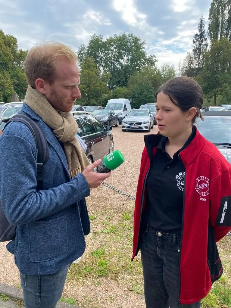 Ein Reporter interviewt eine Jugendliche mit einem Mikrofon auf einem Parkplatz
