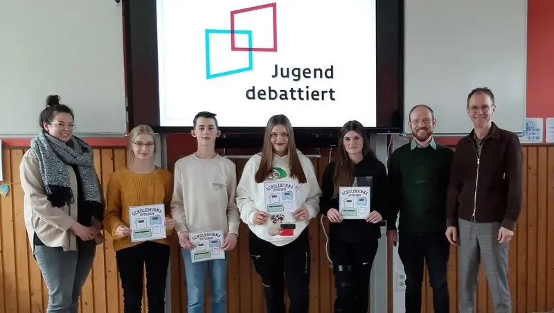 Vier Jugendliche mit Gutscheinen und drei Erwachsene vor einer Leinwand mit „Jugend debattiert“-Logo