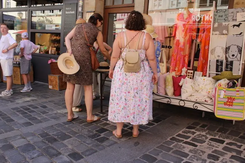 Straßenfotografie: Passantinnen und Passanten vor einem Geschäft mit Taschen und Kleidung auf einer gepflasterten Straße