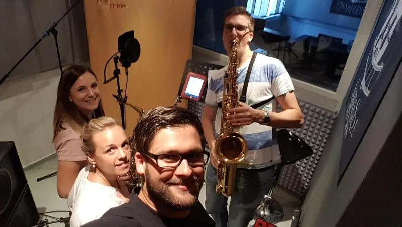 Selfie von vier Erwachsenen im Tonstudio, einer spielt Saxophon