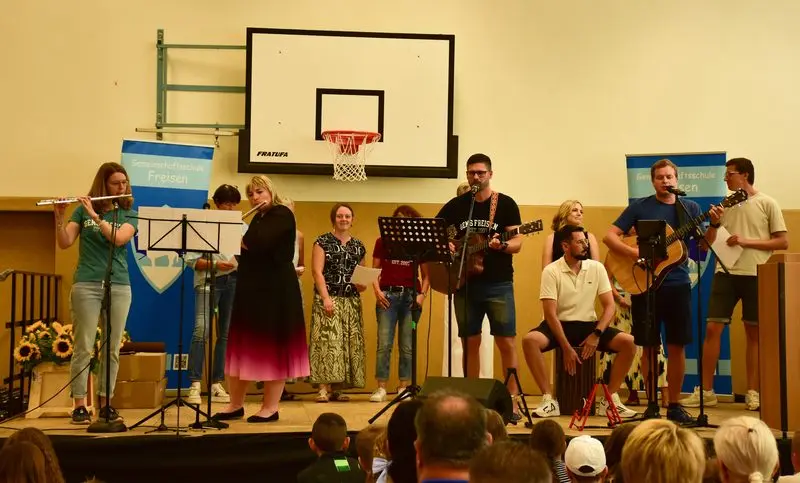Band aus Erwachsenen mit Querflöten, Gitarren, Cajón und Gesang auf der Bühne der Turnhalle bei der Aufnahmefeier