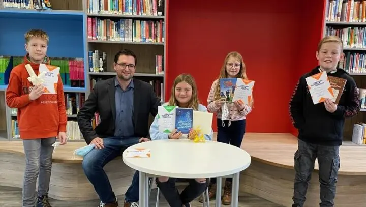 Vier Kinder mit Urkunden und Buchpreisen in der Schülerbibliothek, daneben ein sitzender Erwachsener