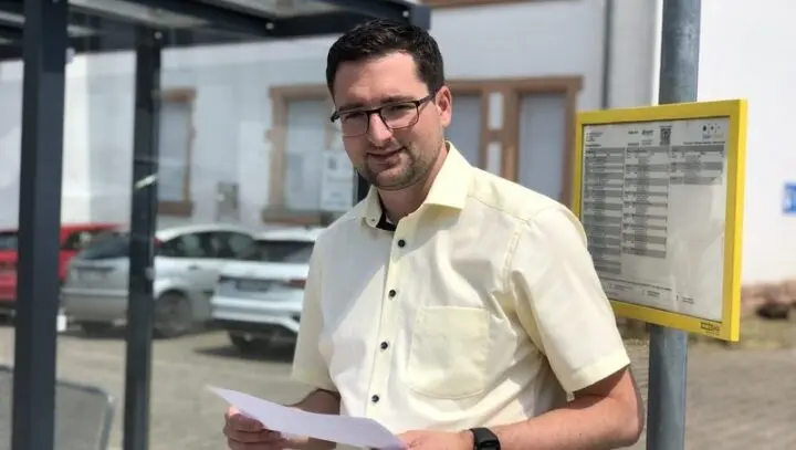 Mann mit einem Blatt Papier an einer Bushaltestelle neben dem Fahrplanaushang