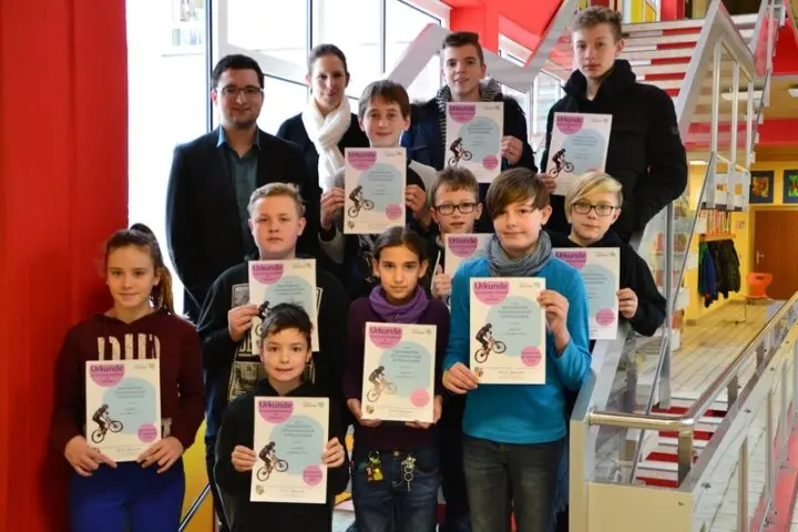 Gruppe von Schülerinnen und Schülern mit Urkunden, dahinter zwei Erwachsene, im Schulgebäude