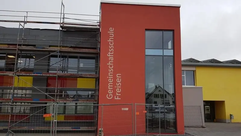 Rot verputzter Gebäudeteil mit Schriftzug „Gemeinschaftsschule Freisen“, daneben eingerüsteter Neubau
