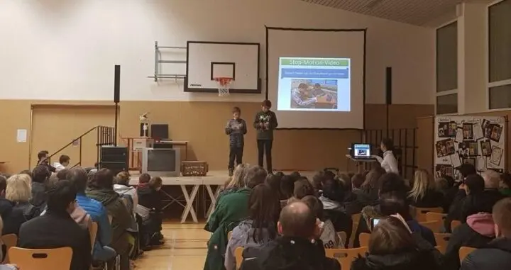 Zwei Schüler präsentieren auf der Bühne ihr Stop-Motion-Video vor Publikum in der Aula