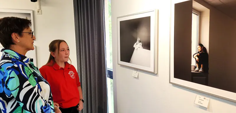 Eine Erwachsene und eine Schülerin betrachten ausgestellte Schwarz-Weiß-Fotos