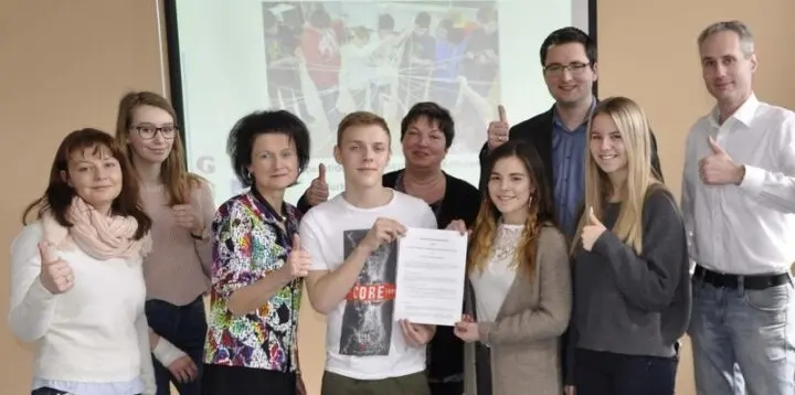 Neun Personen zeigen Daumen hoch, ein Jugendlicher hält ein unterschriebenes Dokument