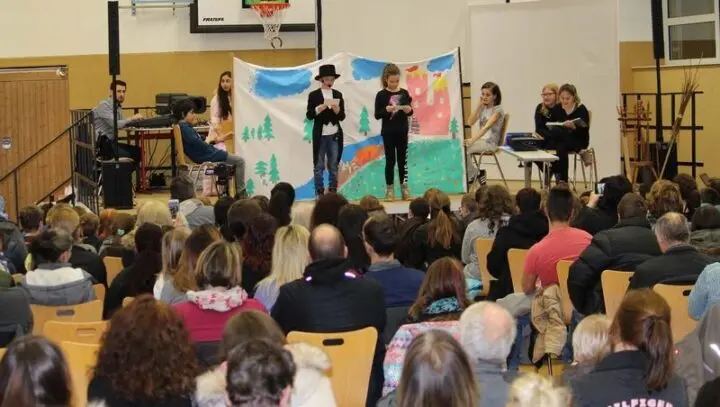 Kinder spielen auf der Bühne vor einer gemalten Märchenkulisse mit Burg, davor das Publikum