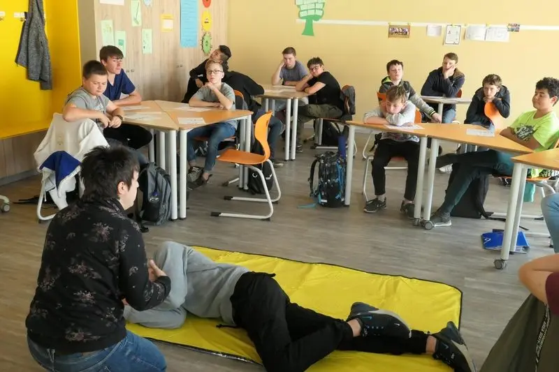 Ausbilderin kniet neben einem Schüler in stabiler Seitenlage, die Klasse schaut zu