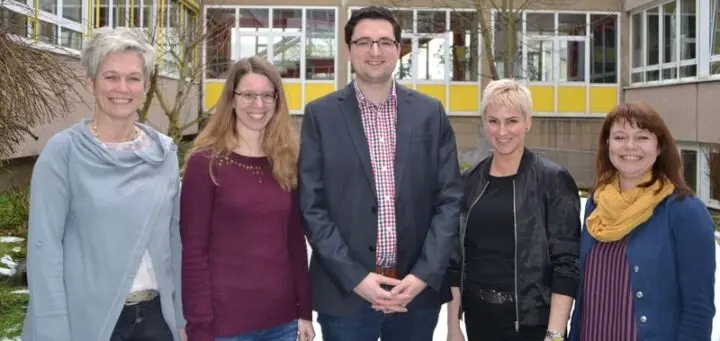 Vier Frauen und ein Mann stehen lächelnd vor dem Schulgebäude