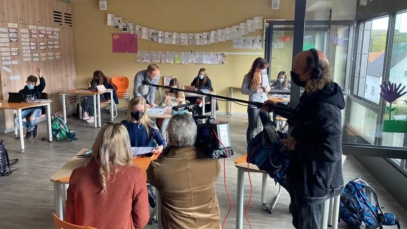 Kamerateam mit Tonangel filmt Schülerinnen und Schüler mit Masken bei der Arbeit im Klassenraum