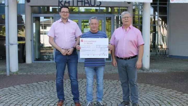 Drei Männer vor dem Rathaus, der mittlere hält einen großen Spendenscheck der Kreissparkasse St. Wendel