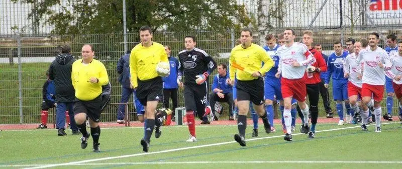 Schiedsrichter in gelben Trikots laufen mit zwei Fußballmannschaften aufs Spielfeld