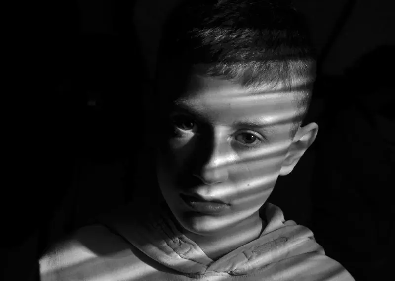Schwarz-Weiß-Porträt eines Jungen, über dessen Gesicht Lichtstreifen wie von einer Jalousie fallen