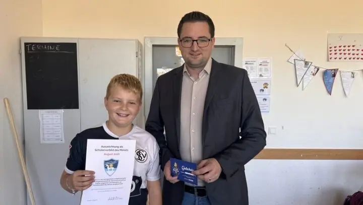 Schüler hält Urkunde „Auszeichnung als Schülervorbild des Monats August 2026“, daneben ein Mann mit Gutschein