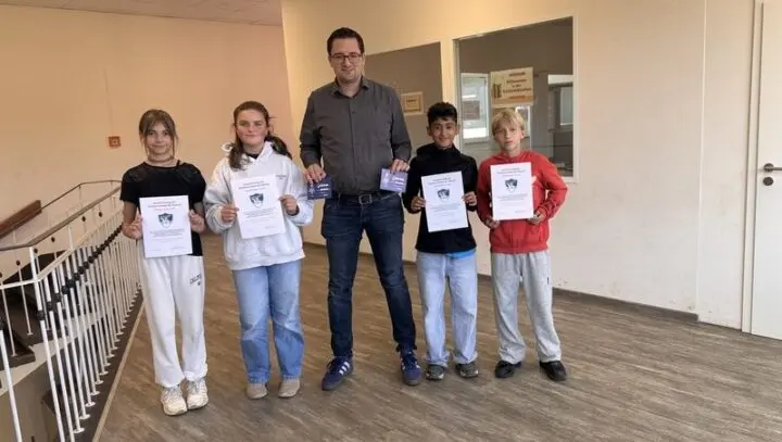 Vier Schülerinnen und Schüler mit Urkunden und Gutscheinen, in der Mitte ein Mann, im Schulflur