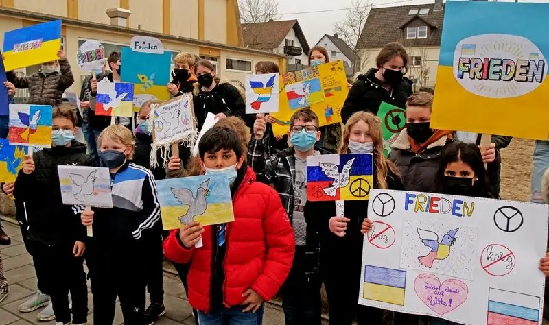 Kinder mit Masken halten Plakate mit Friedenstauben und „Frieden“ in Blau-Gelb
