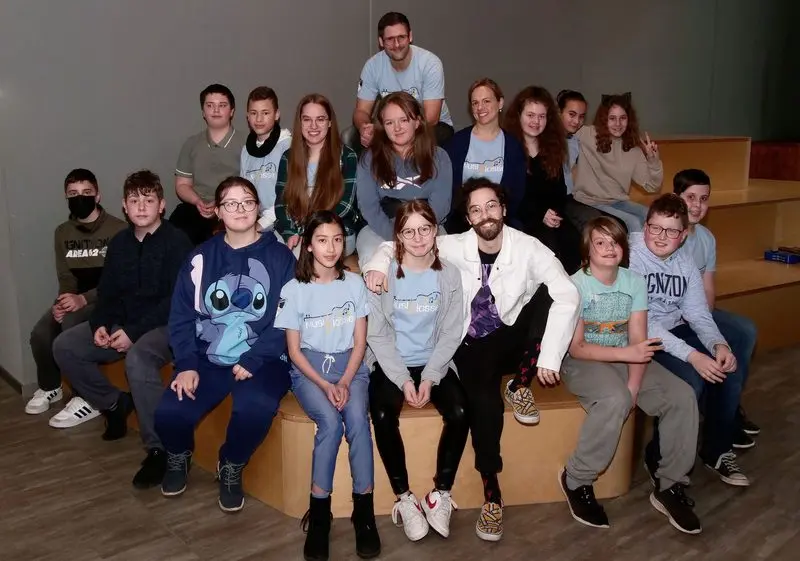 Gruppenfoto von Jugendlichen und Erwachsenen auf einer Sitztreppe, viele in hellblauen MusiKlasse-T-Shirts