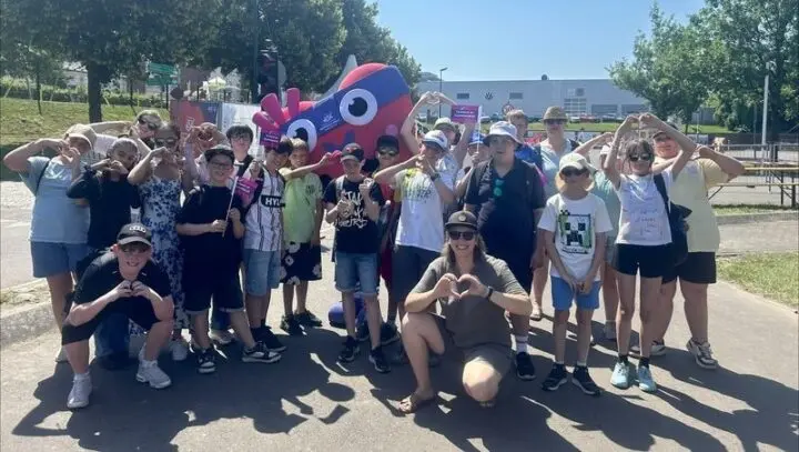 Klassengruppe formt Herzen mit den Händen vor einer Maskottchen-Figur im Freien