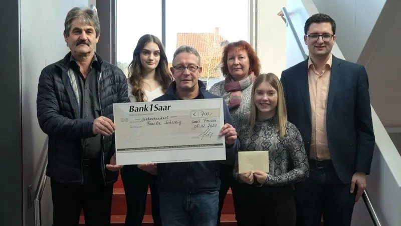 Sechs Personen halten einen Spendenscheck der Bank 1 Saar über 700 Euro, eine Jugendliche hält einen Umschlag