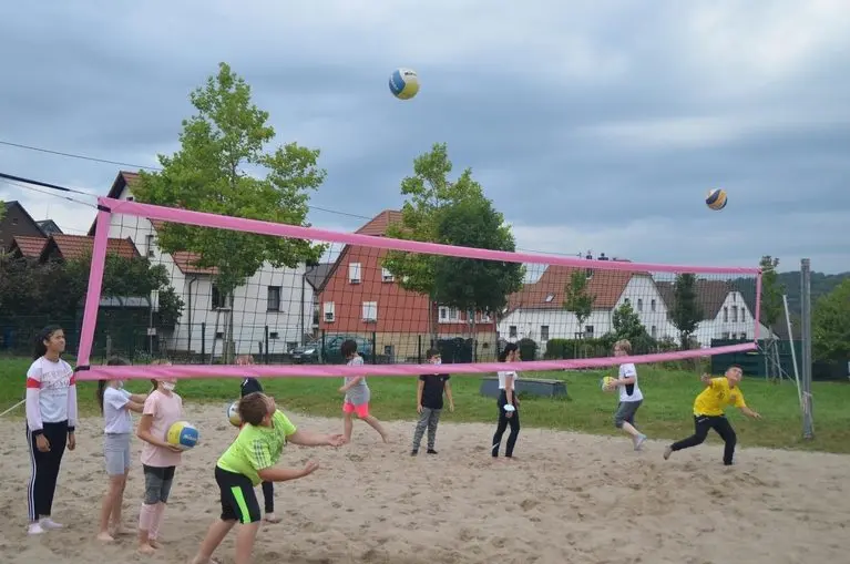 Jugendliche spielen Volleyball auf einem Sandplatz mit pinkfarbenem Netz