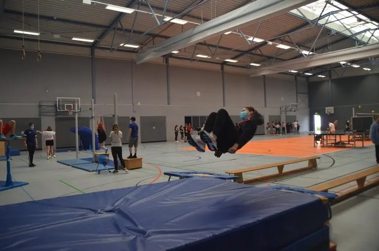 Sporthalle mit Turngeräten; eine Schülerin springt auf eine Weichbodenmatte