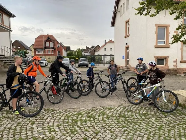 Gruppe Jugendlicher mit Fahrrädern und Helmen auf einem gepflasterten Platz
