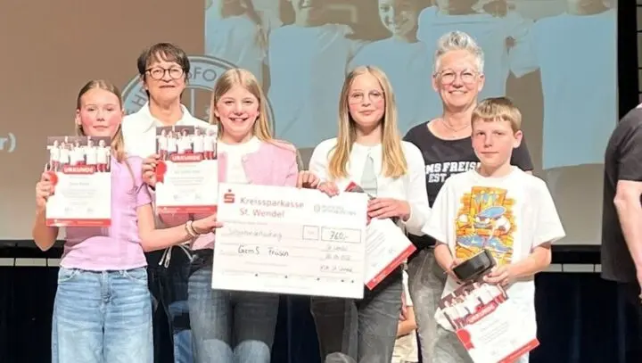 Schülerinnen, ein Schüler und zwei Erwachsene auf einer Bühne mit Urkunden und Scheck der Kreissparkasse über 760 Euro