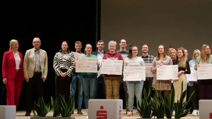 Zahlreiche Erwachsene stehen auf einer Bühne und halten Schecks der Kreissparkasse St. Wendel