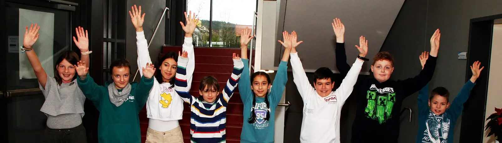 Kinder stehen nebeneinander vor einer Treppe und strecken die Arme nach oben