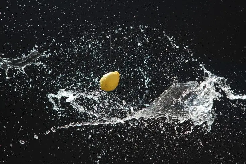 Fotografie: Zitrone fällt in Wasser, Spritzer vor schwarzem Hintergrund