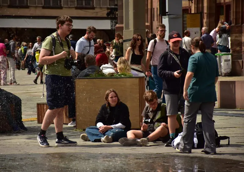Jugendliche mit Kameras sitzen und stehen auf einem belebten Platz in einer Altstadt