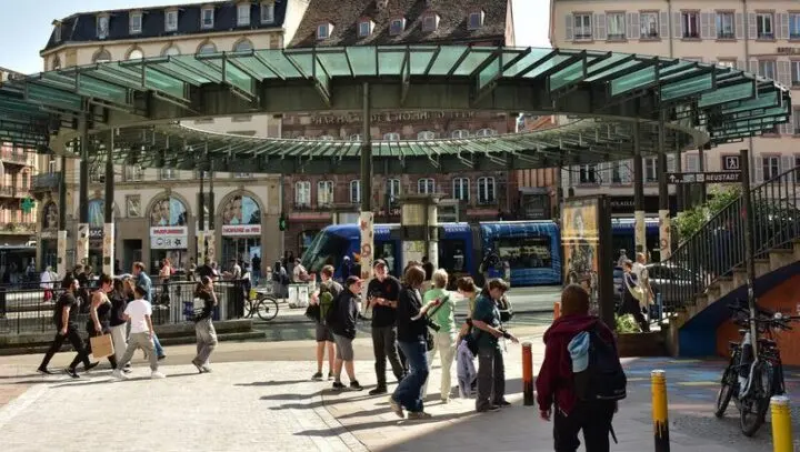 Gruppe mit Kameras an einer Straßenbahnhaltestelle mit großem Glasdach, dahinter eine Tram