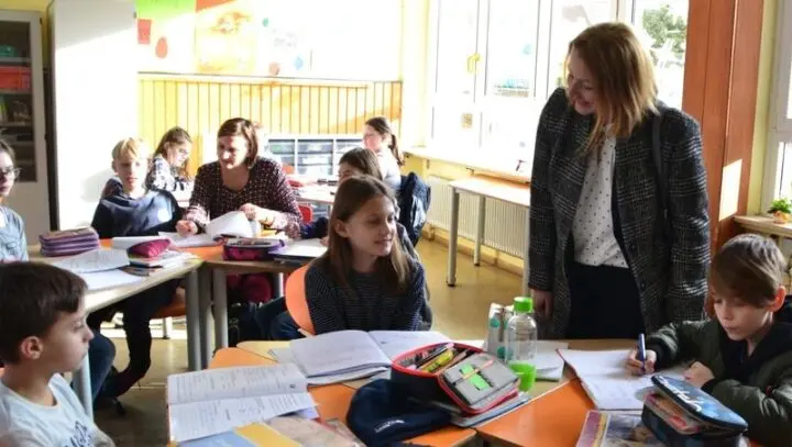 Besucherin im Gespräch mit Schülerinnen und Schülern an ihren Tischen im Klassenraum