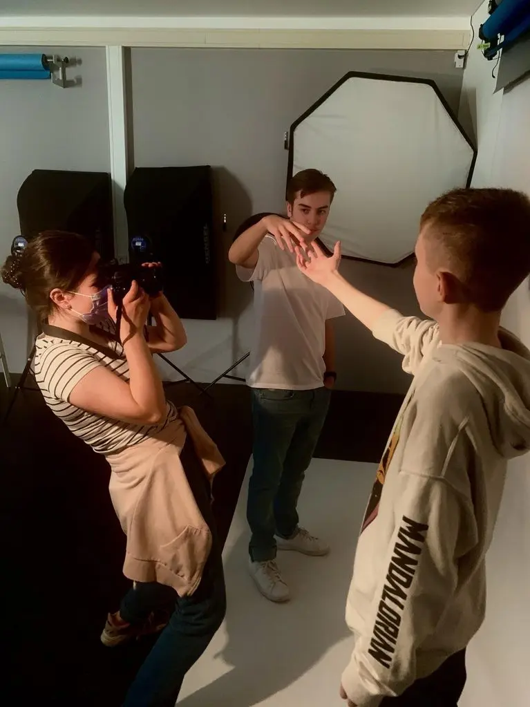 Im Fotostudio fotografiert eine Jugendliche zwei Jungen, die ihre Hände vor Softboxen inszenieren