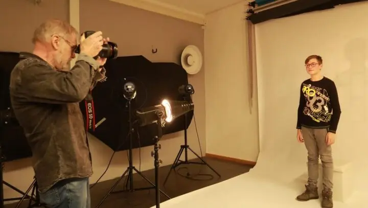 Mann fotografiert einen Jungen vor weißem Studiohintergrund, umgeben von Studioleuchten