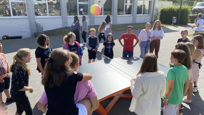 Schülerinnen und Schüler stehen um eine Teqball-Platte auf dem Schulhof, ein Ball fliegt