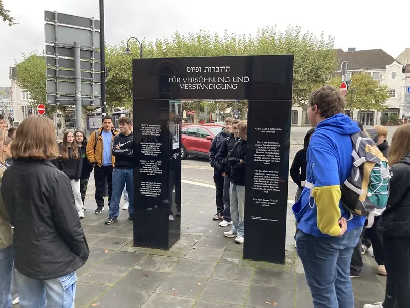 Jugendliche an einem schwarzen Mahnmal mit der Inschrift „Für Versöhnung und Verständigung“
