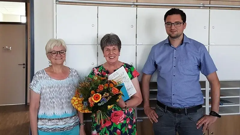 Frau mit Blumenstrauß und Karte bei der Verabschiedung, neben ihr zwei weitere Erwachsene