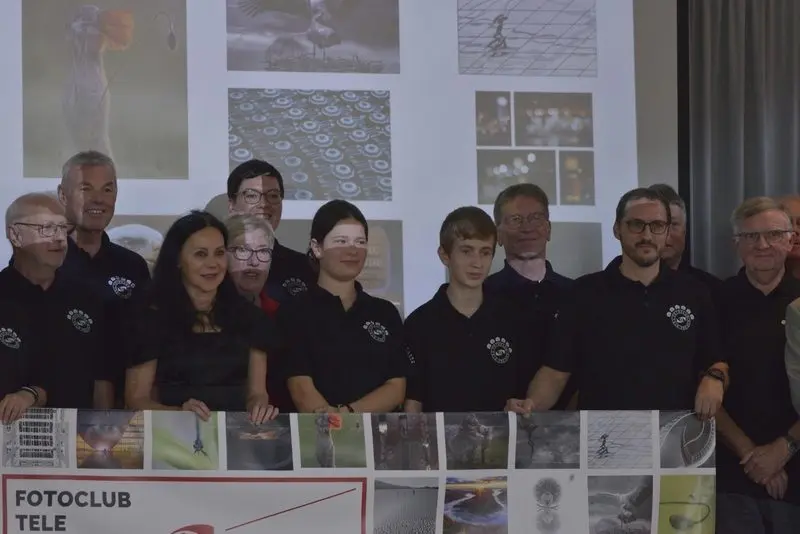 Mitglieder des Fotoclubs Tele in schwarzen Poloshirts hinter einem Banner mit Fotos